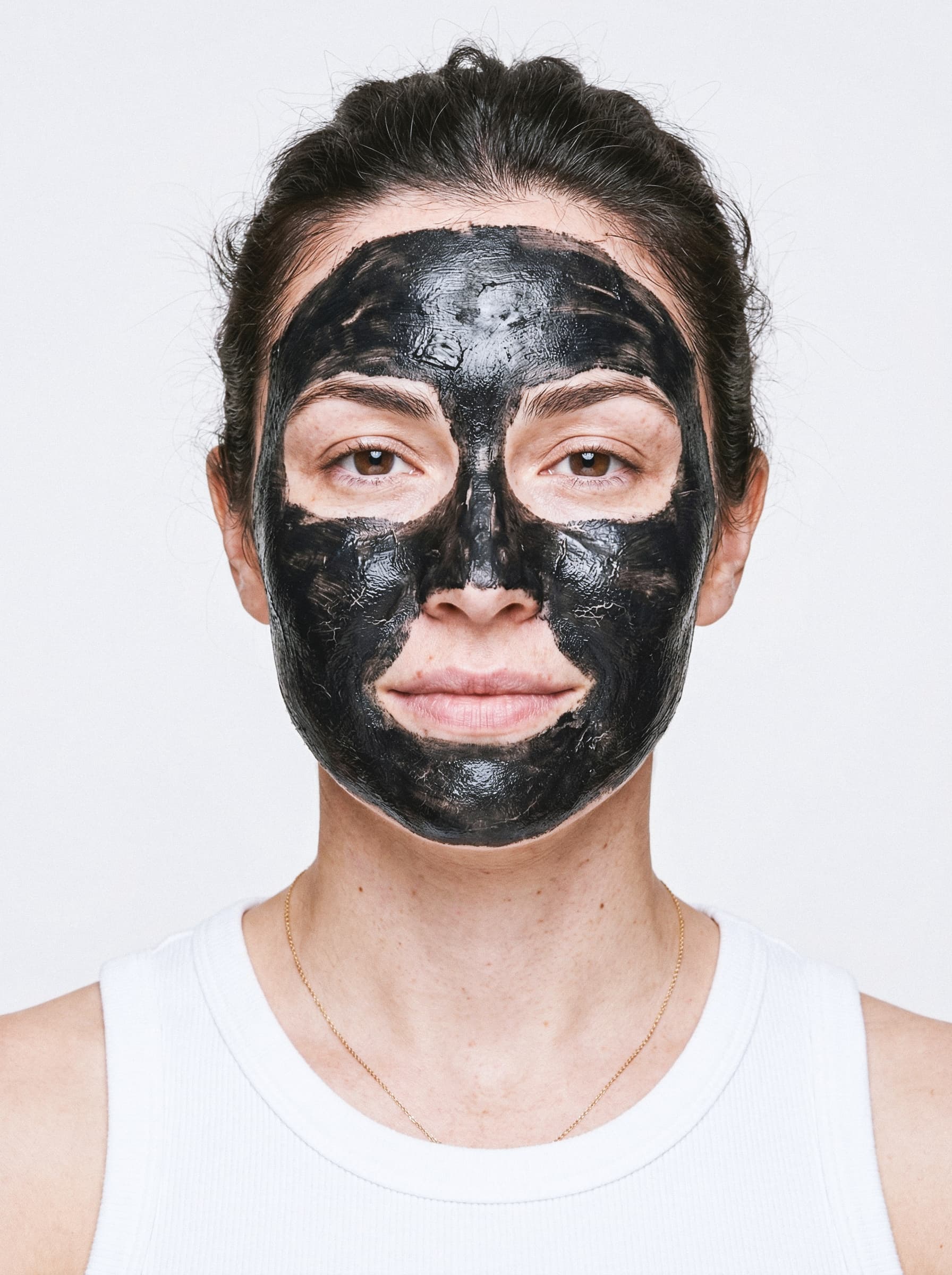 Premium beauty campaign photography showcasing a model applying a black charcoal clay mask for R\AW mineral skincare brand
